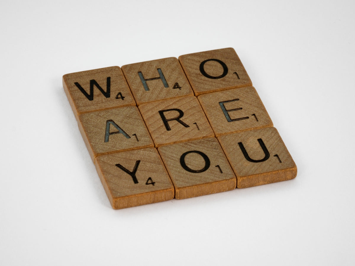 Wooden Scrabble tiles arranged in a grid spelling the words WHO ARE YOU